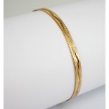 A gold coloured bangle, of oval form with engine turned decoration to exterior, stamped ?18K? to