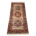 A Caucasian wool pile rug, the three red and blue alternating medallions upon an ivory ground,