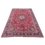 A hand woven Persian Mashad carpet, with multi-coloured floral medallion against a red ground,