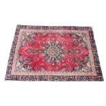 A vintage washed red ground Persian Heriz rug, with a traditional geometric design, the central