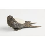 A novelty pin cushion in the form of a swallow, feather effect chasing and glass eyes, cream