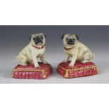 A pair of Halcyon Days pugs, modelled seated on cushions, with printed marks to base, 9.5cm high (2)