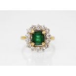 An emerald and diamond 18ct gold cluster ring, the central rectangular step cut emerald measuring