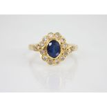 A sapphire and diamond 18ct gold cluster ring, the central oval mixed cut sapphire measuring 6.5mm x