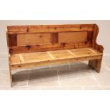 A pine settle, 20th century, the panelled back above a board seat upon shaped end supports, 99cm H x
