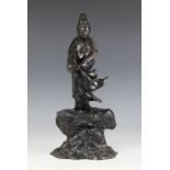 A Chinese bronze model of Guanyin, 19th century, modelled standing in a flowing robe upon a rocky