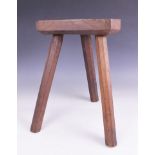 An elm jointed milking stool, the canted slab seat raised upon a trio of octagonal chamfered legs,