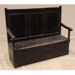A 17th century oak box settle, the three panel back rest flanked by down swept arm rests raised upon