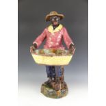A late 19th century continental majolica blackamoor, modelled as a man standing holding a basket,