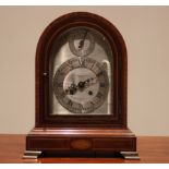 An early 20th century mahogany cased mantel clock, the arched case with oval fan inlay enclosing the
