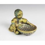 A Zsolnay Pecs (Hungary) green lustre model of a girl, designed seated besides a woven basket,