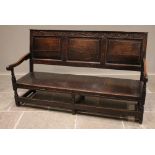A George III oak settle, the three panel back with a foliate carved frieze above the board seat,