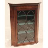 An early 19th century glazed mahogany hanging corner cupboard, the moulded cornice above a plain