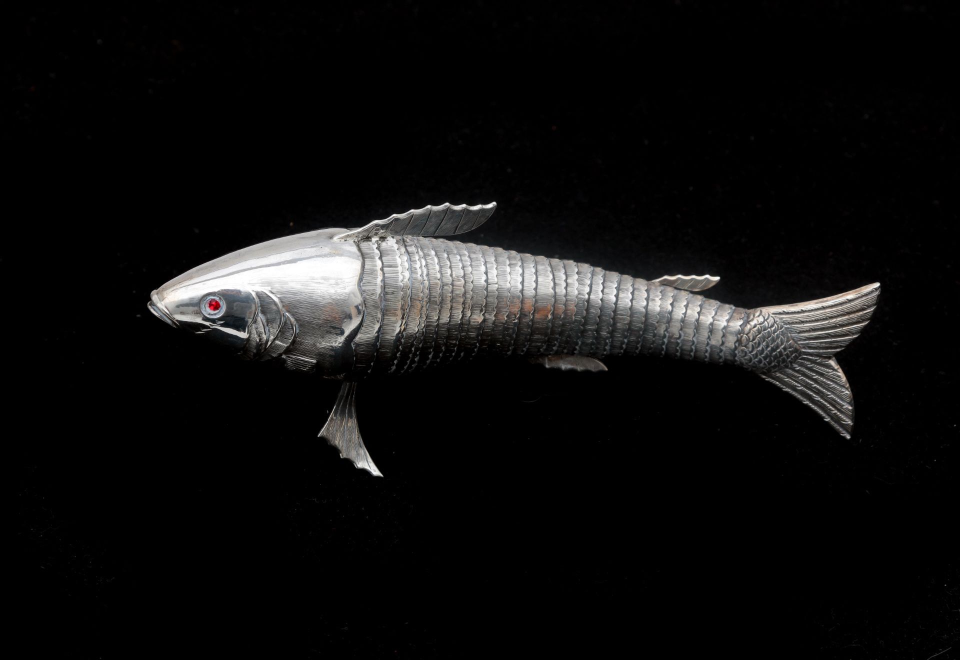 A silver table centerpiece in the shape of a fish, with a movable body, and red glass faceted cut