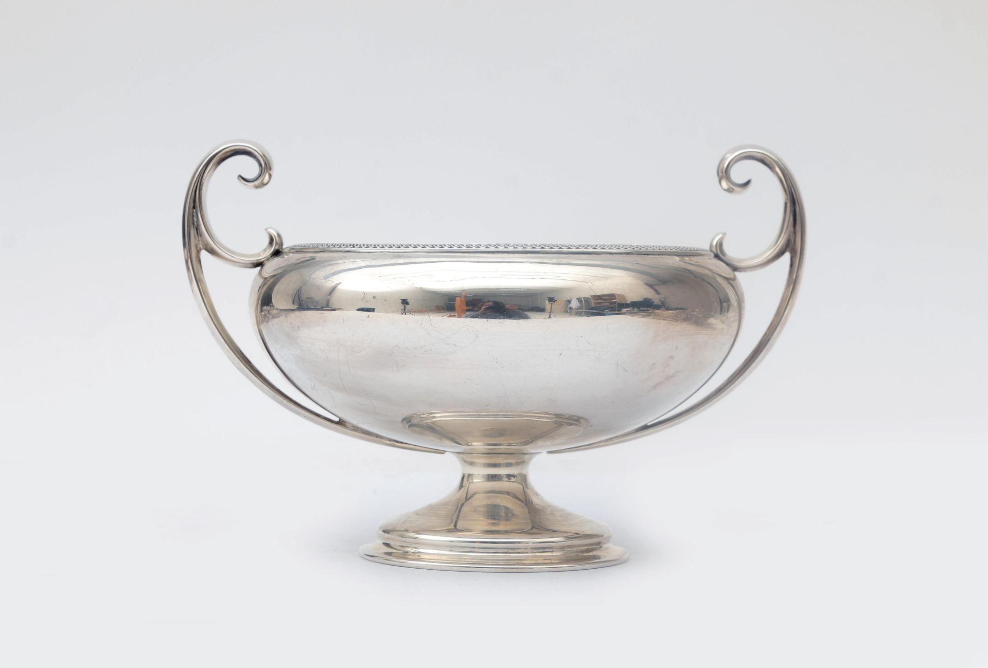 A sterling silver cream bowl on a foot, a round wide-flaring bowl with two high, upright curling