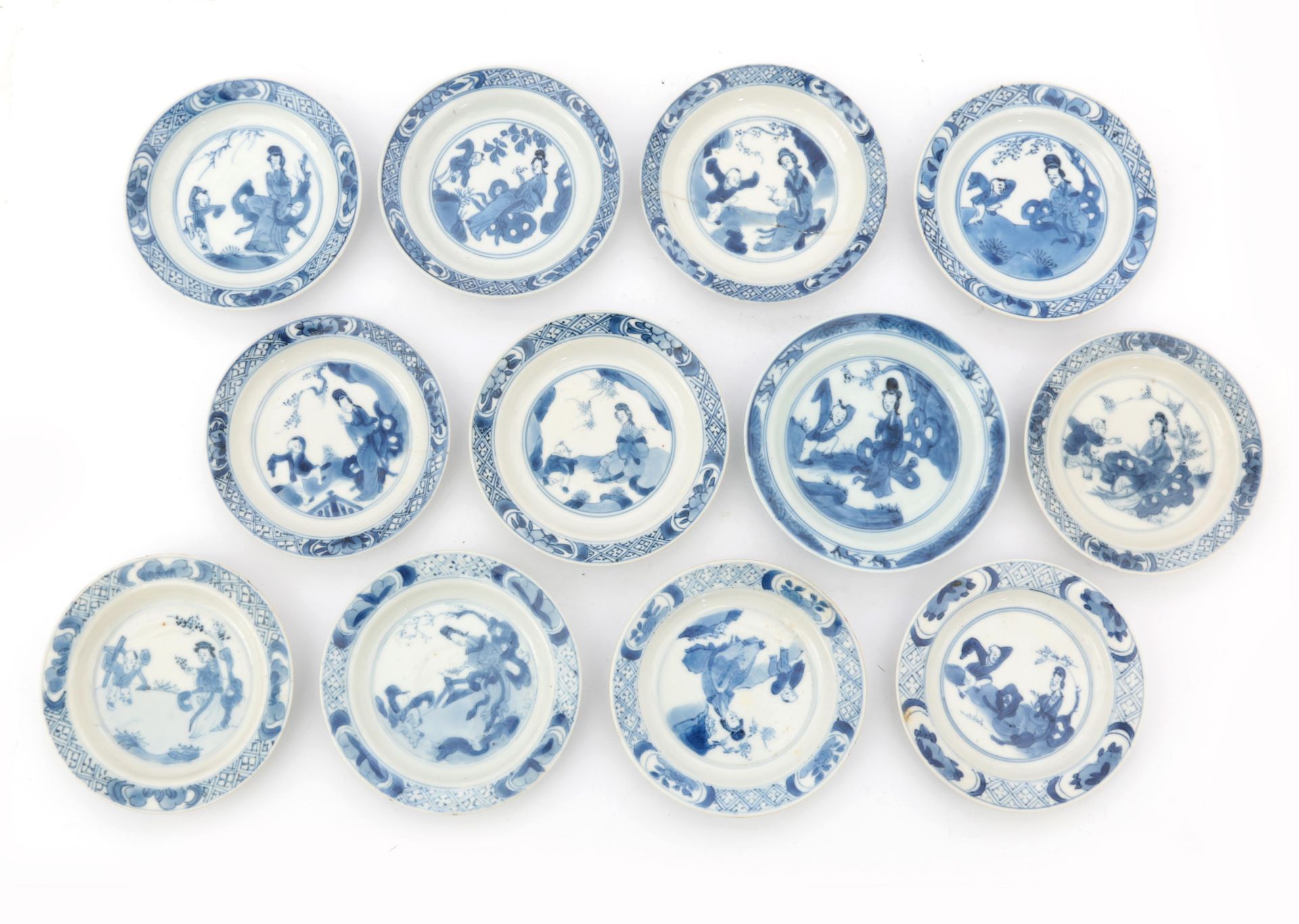 Twelve Chinese porcelain dishes, decorated with a playing child and a woman in a garden in Kangxi-