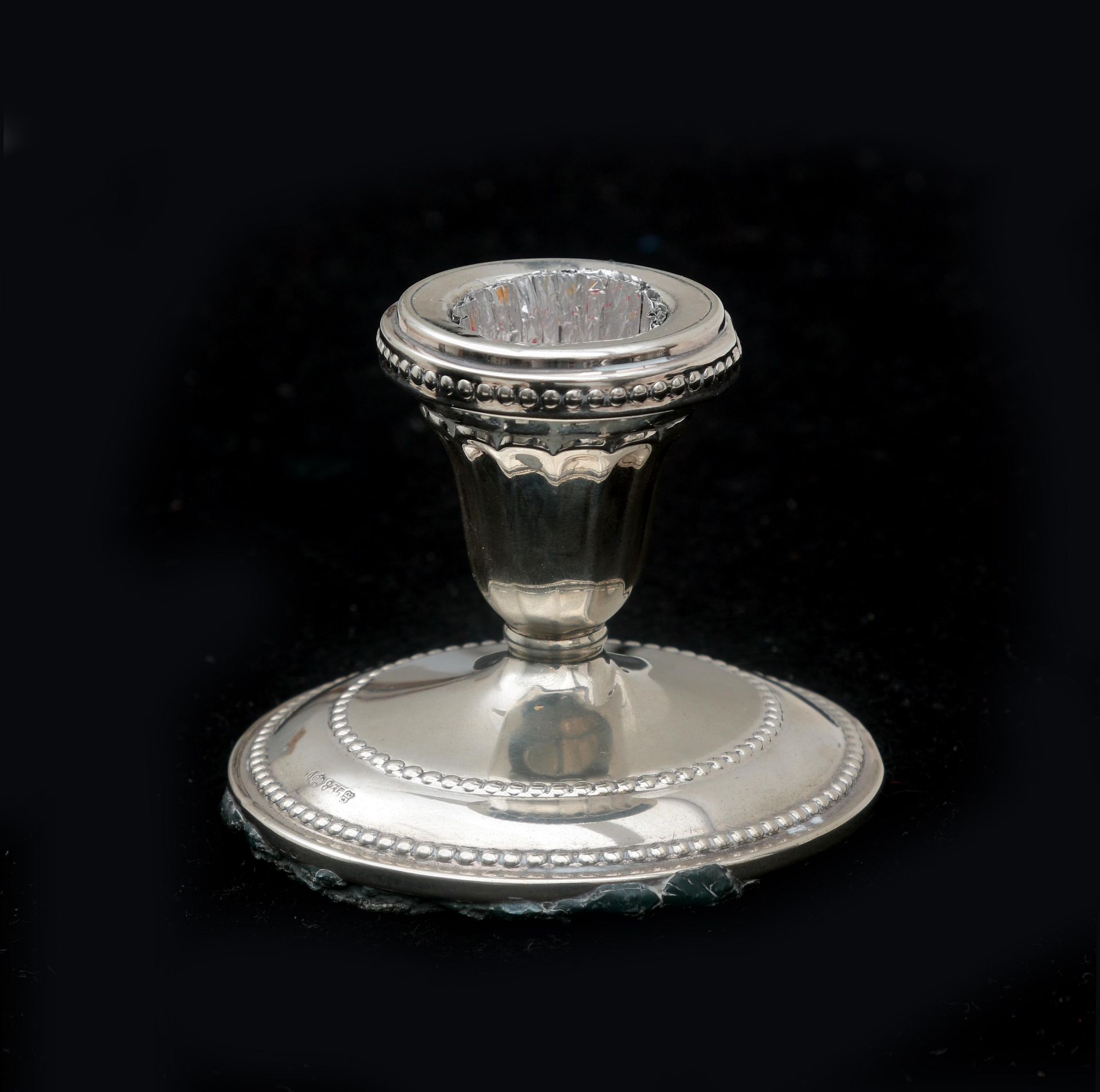 A silver candlestick on a round foot with a pearl rim. With traces of use and slightly loosened