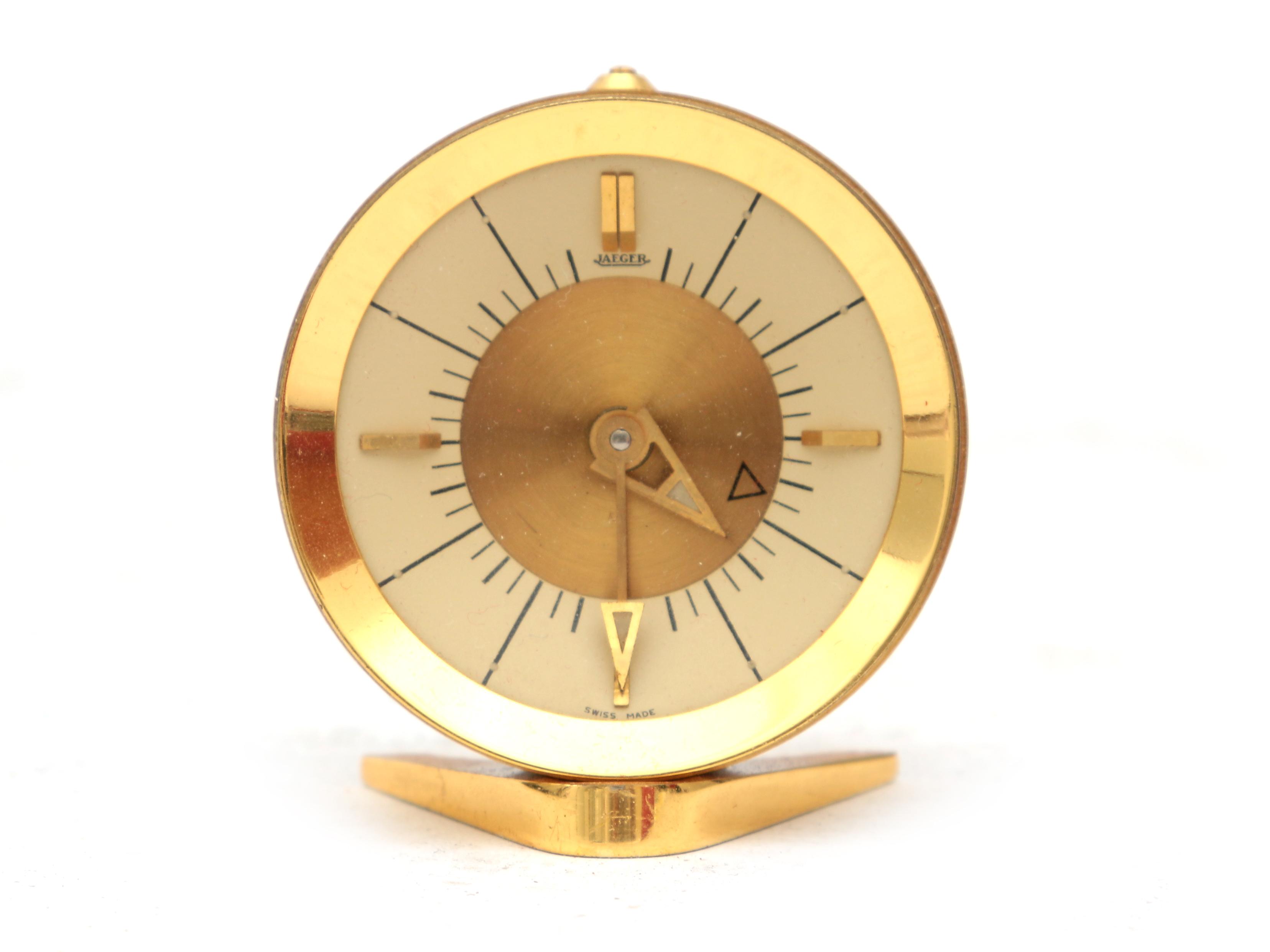 Jaeger A gilt brass travel alarm clock in red box, midcentury, marked to the dial. 5 cm. h.