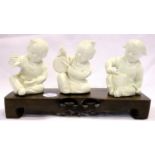 Three Oriental ceramic figurines of young children with musical instruments on a wooden plinth, L: