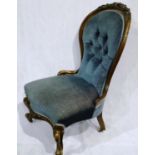 A Victorian low seated parlour chair with heavily carved walnut frame and later buttoned upholstery.