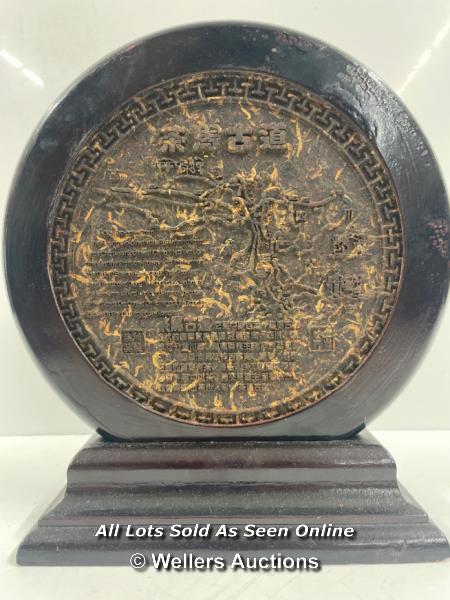 A CIRCULAR CHINESE COMPRESSED TEA BLOCK, 25.5CM HIGH (ON STAND) 23.5CM DIAMETER