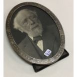 An oval silver picture frame with engraved decorat