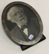 An oval silver picture frame with engraved decorat