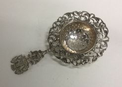 A pierced silver tea strainer with armorial decora