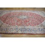 +VAT A 20th century carpet, possibly silk blend, the red ground richly decorated with floral
