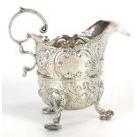 A Victorian silver cream jug with leaf capped c-scroll handle and repousse decorated body on three