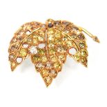 A yellow metal brooch of vine leaf form set white, yellow and cinnamon diamonds within recessed