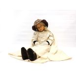 An early 20th century fabric doll with painted pressed canvas head and wearing embroidered clothing,