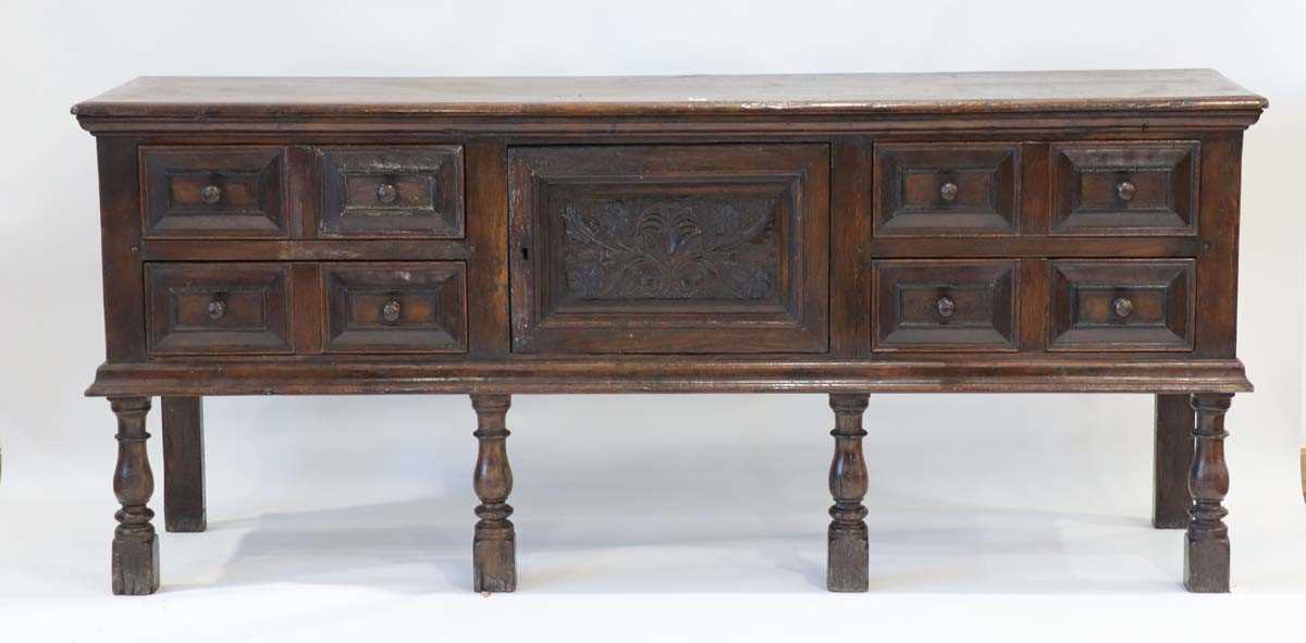 An oak dresser base incorporating 17th century elements, the central carved panelled door flanked by