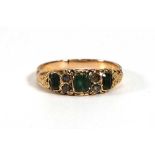 An early 20th century yellow metal ring set three square cut emeralds and three small diamonds in