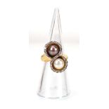 A yellow metal crossover ring set grey and white pearl within a border of small diamonds, ring