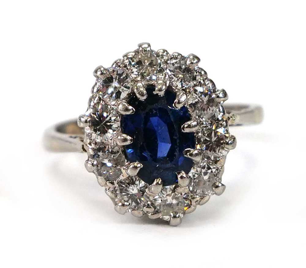 A white metal cluster ring set oval pale blue sapphire within a border of ten brilliant cut