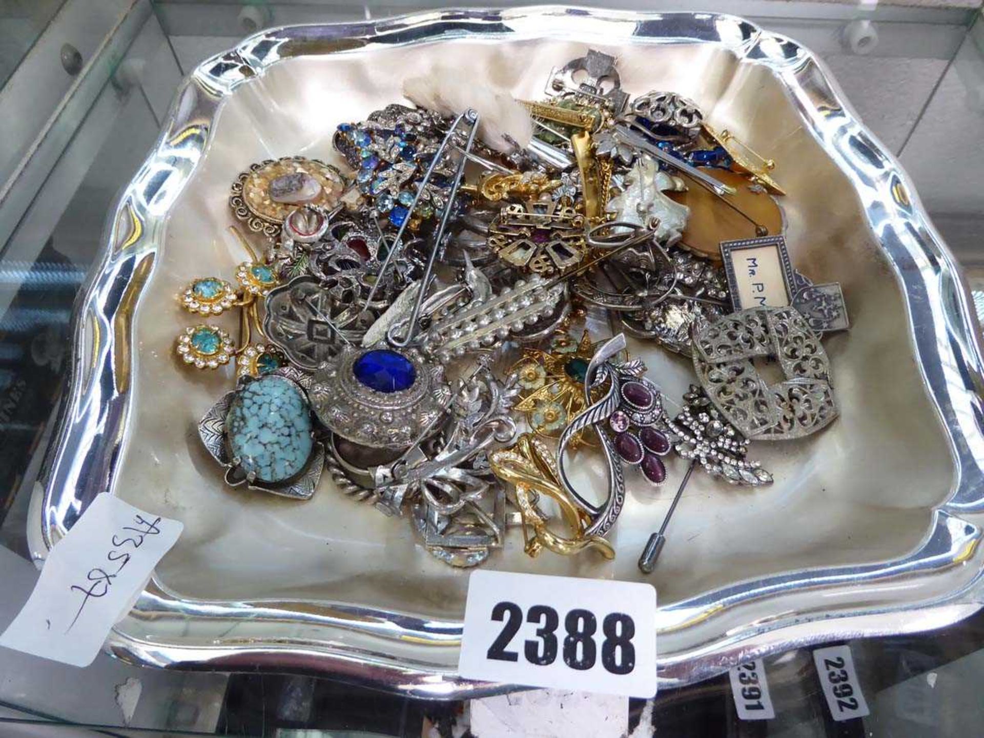 White metal tray containing various brooches, badges and other costume jewellery items