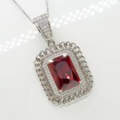 A large step-cut red cubic zirconia pendant and chain with a white cubic zirconia halo in silver