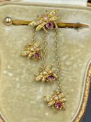 A gold brooch with a bee theme with rubies and seed pearls