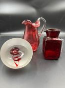 A selection of cranberry glass to include paperweights and jugs