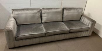 A three seater modern classic elegant sofa with silver upholstery plush cushions and over lapping