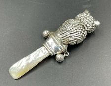 A silver and mother of pearl teething ring in the form of an owl with glass eyes.