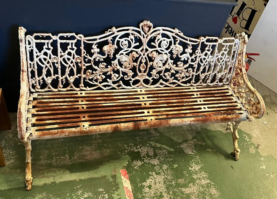 An architectural cast iron bench with vine pattern cast back, scrolling arms and iron slat seats,