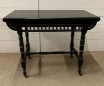 An ebonised aesthetic card table, opening up to a red baize interior on turn legs and castors (H73cm