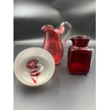 A selection of cranberry glass to include paperweights and jugs