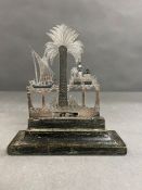 A silver cut out of a tropical scene mounted on a wooden plinth