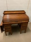 An oak roll top desk, opening to reveal drawers and pigeon holes (H110cm W113cm D72cm)