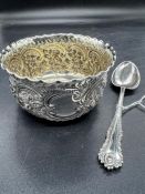 A cased silver porringer and spoon with scroll and floriate repousse decoration with gilded bowl