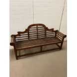 A teak slatted garden Lutyens style bench with scrolled ends and sloping arches