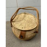 A wicker lidded basket with rope handles and leather strapping